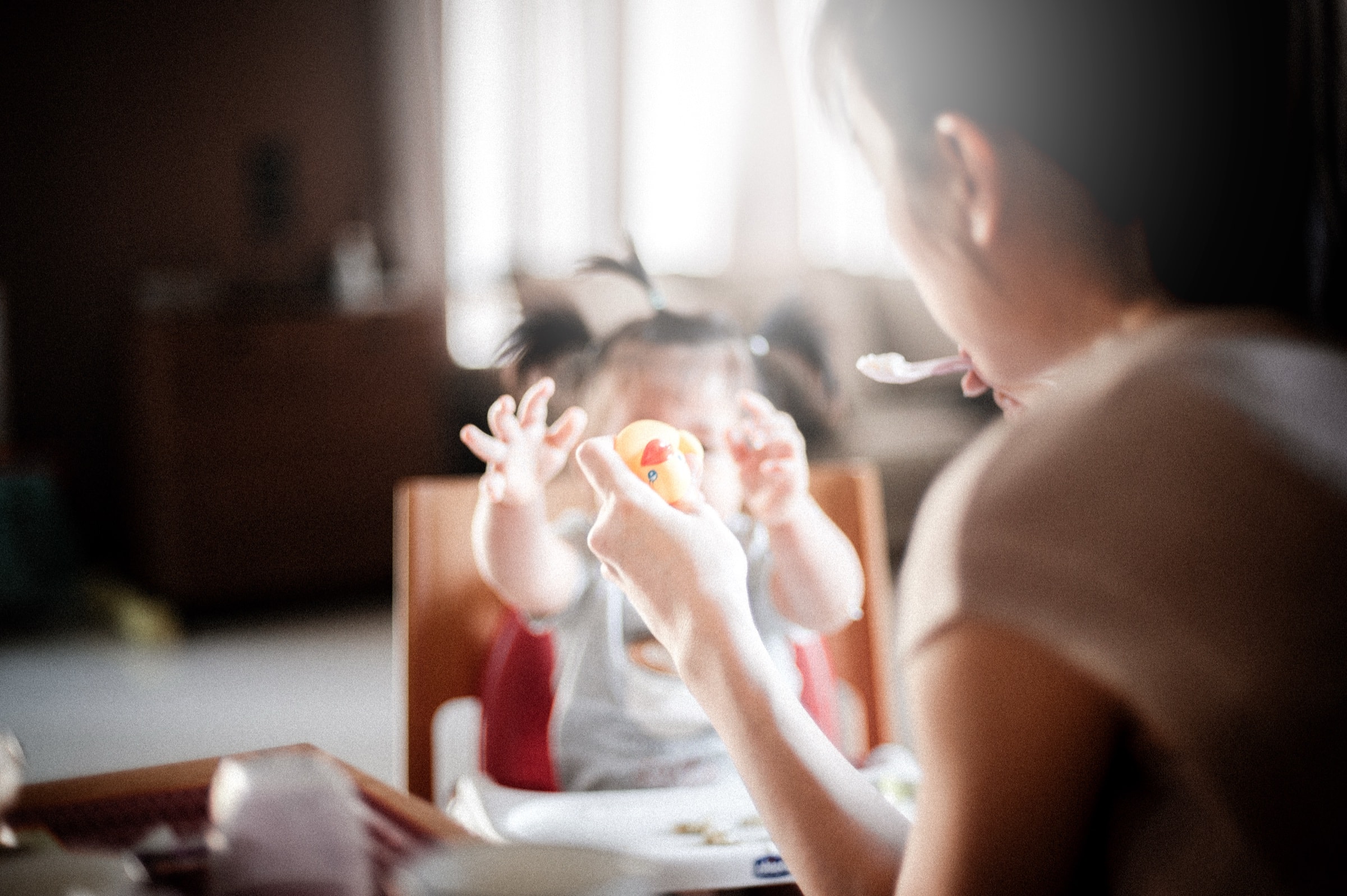 A baby reaching up towards a parent's hands in soft window light