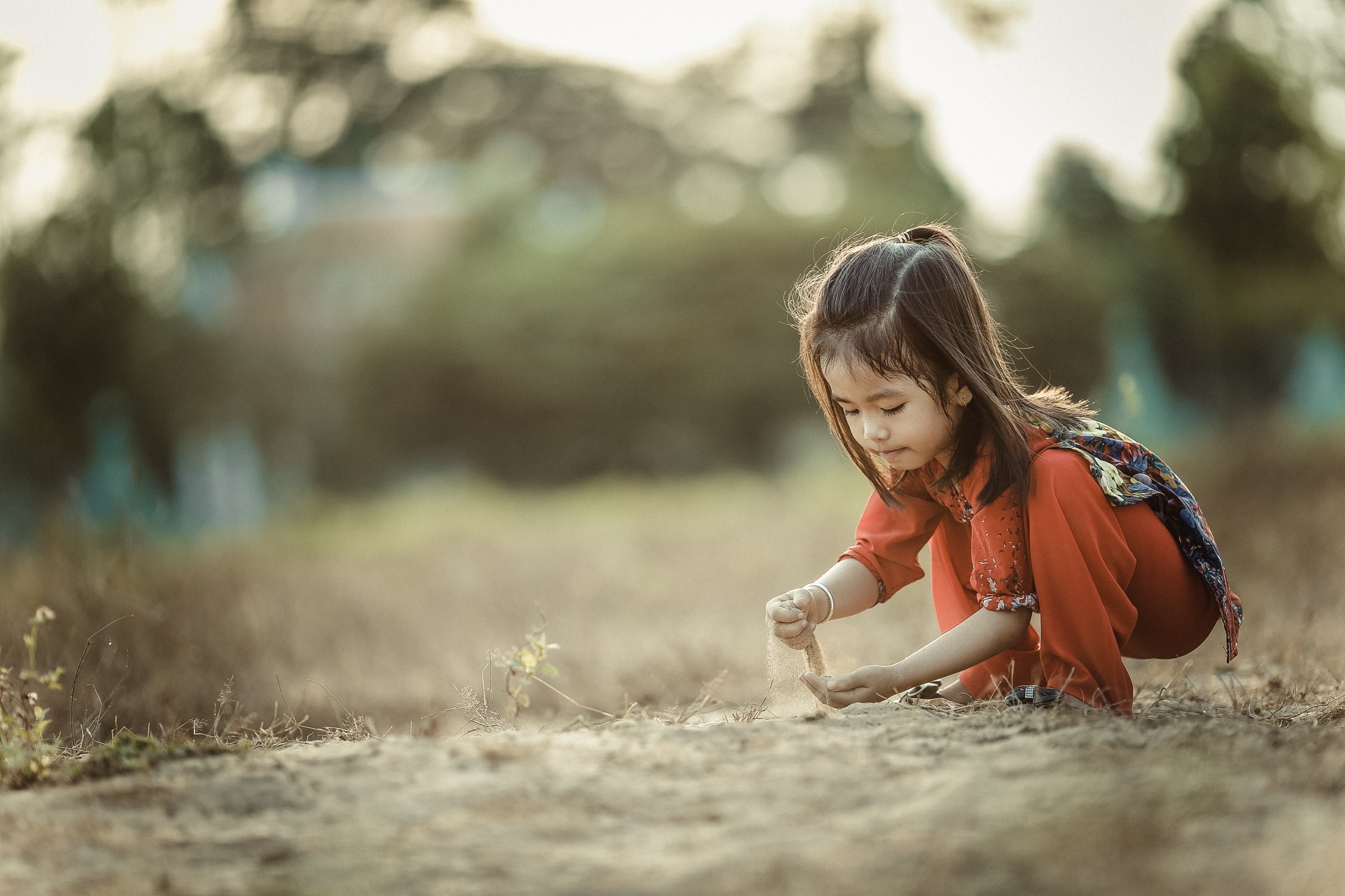 A child kneeling to play in the sand outdoors