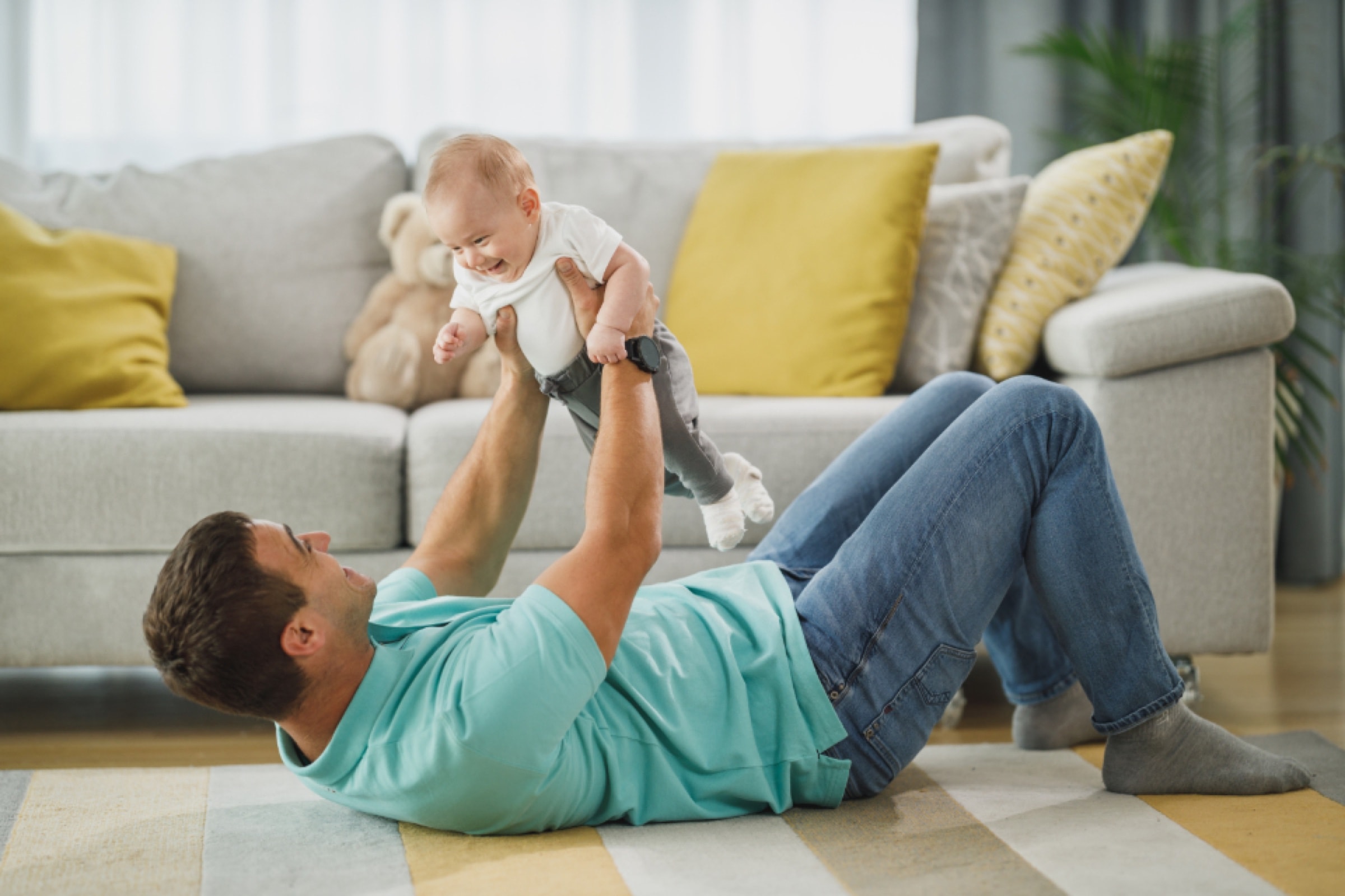 A father lying on the floor lifting his baby above him