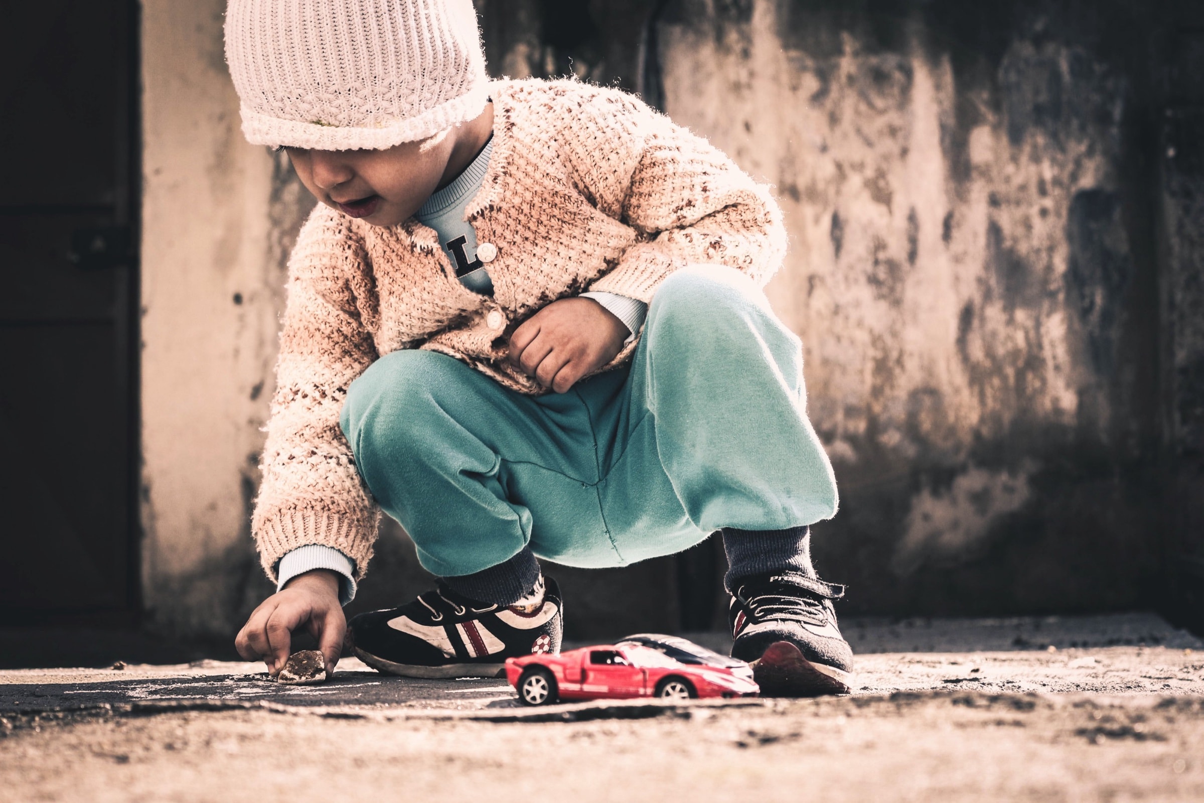 A toddler crouched over a toy car on the pavement