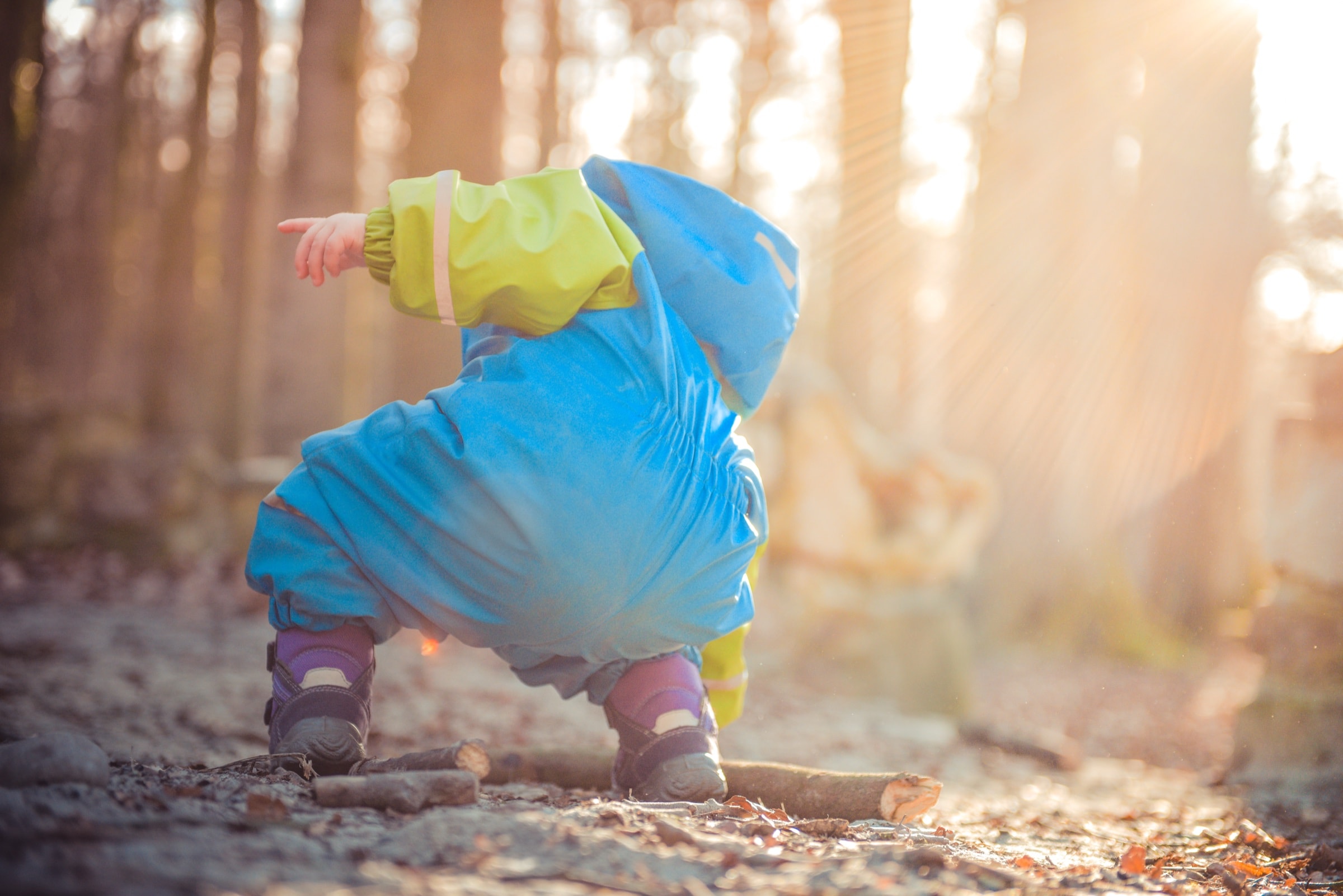 A toddler in a blue coat crouching down to look at something outdoors