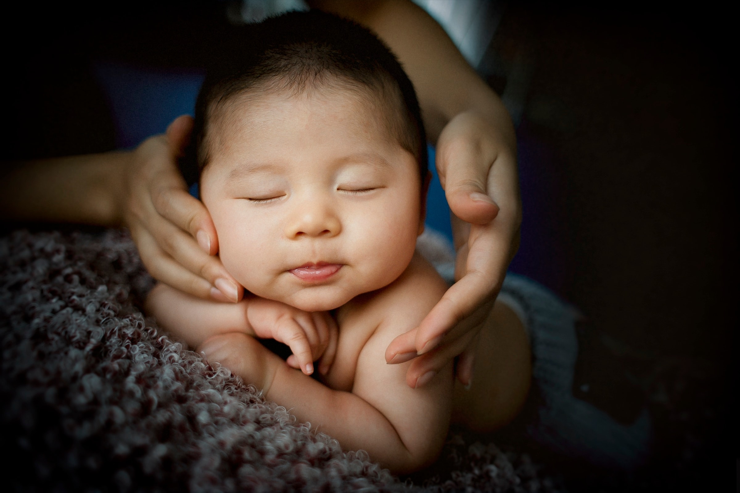 A baby asleep in a parent's cupped hands