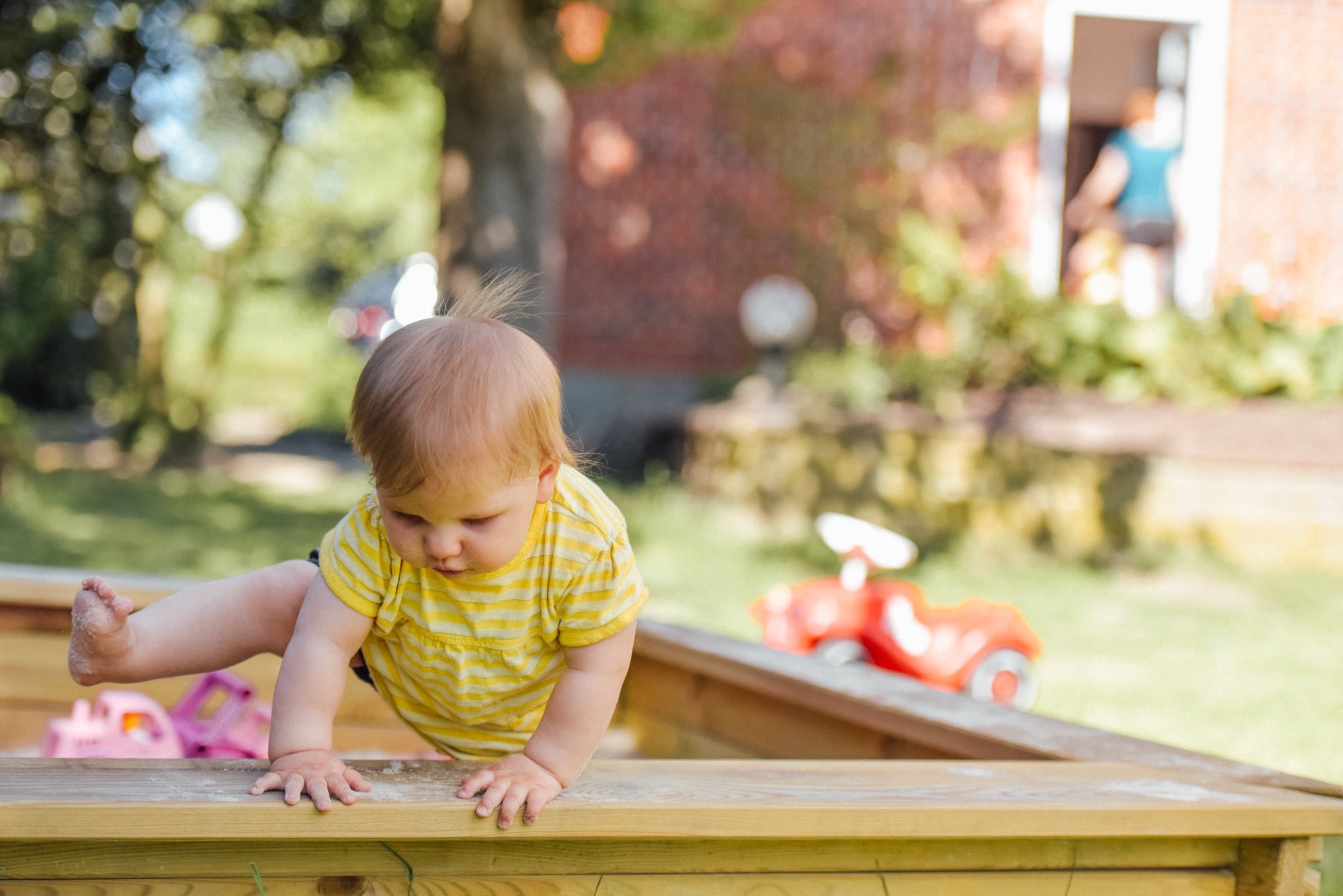 A baby sitting at the edge of a sandpit in a garden