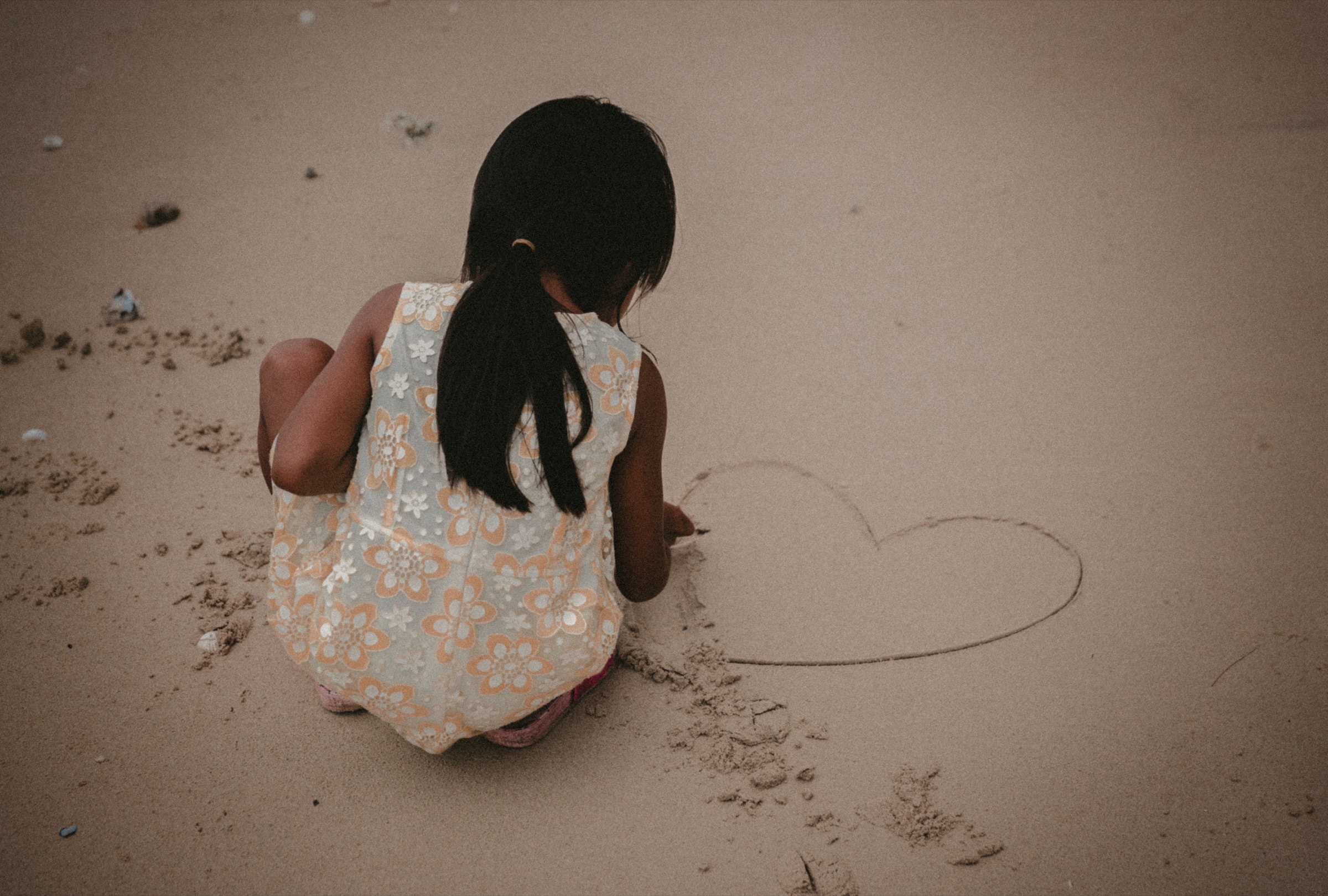 A child drawing a heart in the sand