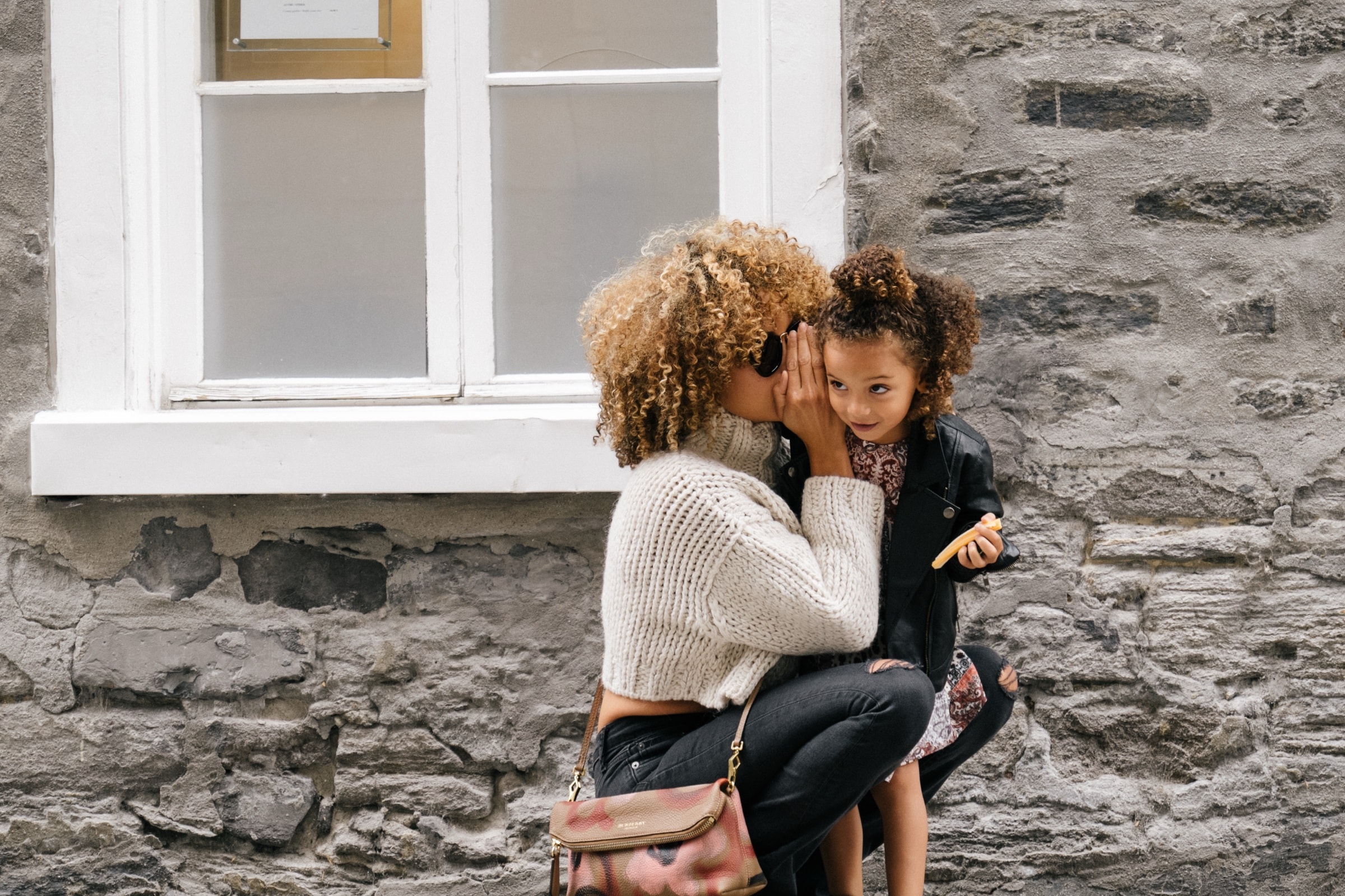 A mother holding two children outside a stone house