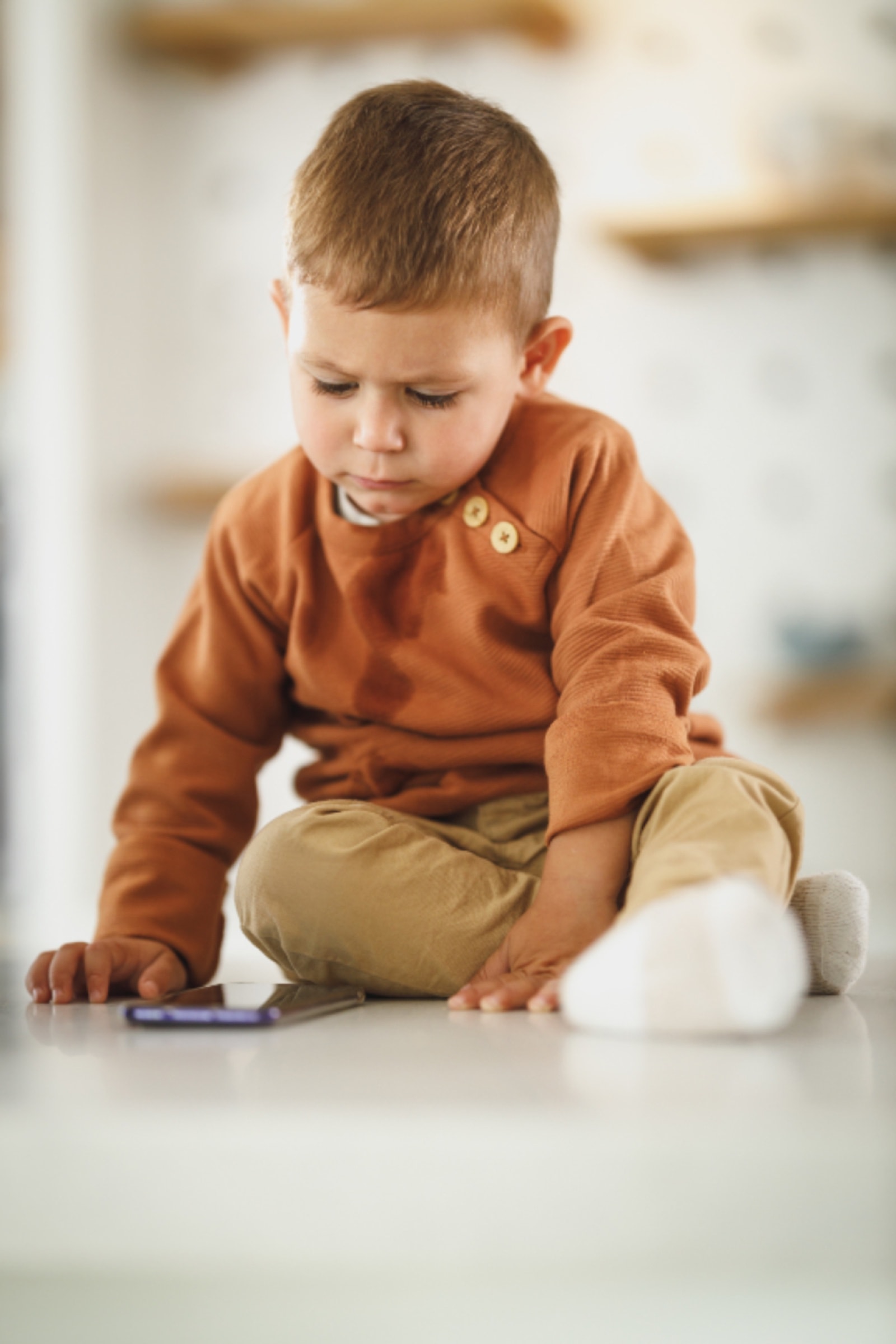A toddler in an orange jumper sitting absorbed in play