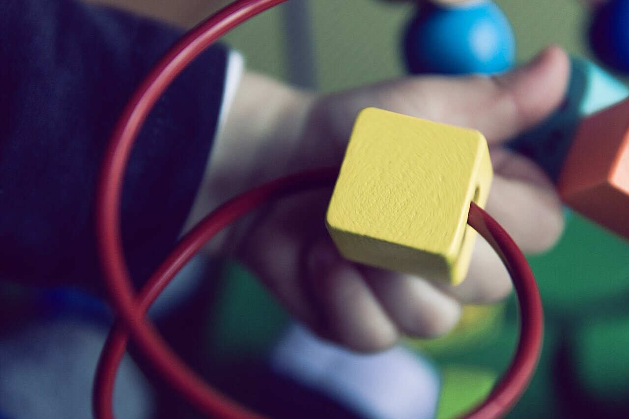 A toddler's hand holding a yellow wooden bead on a wire bead maze toy