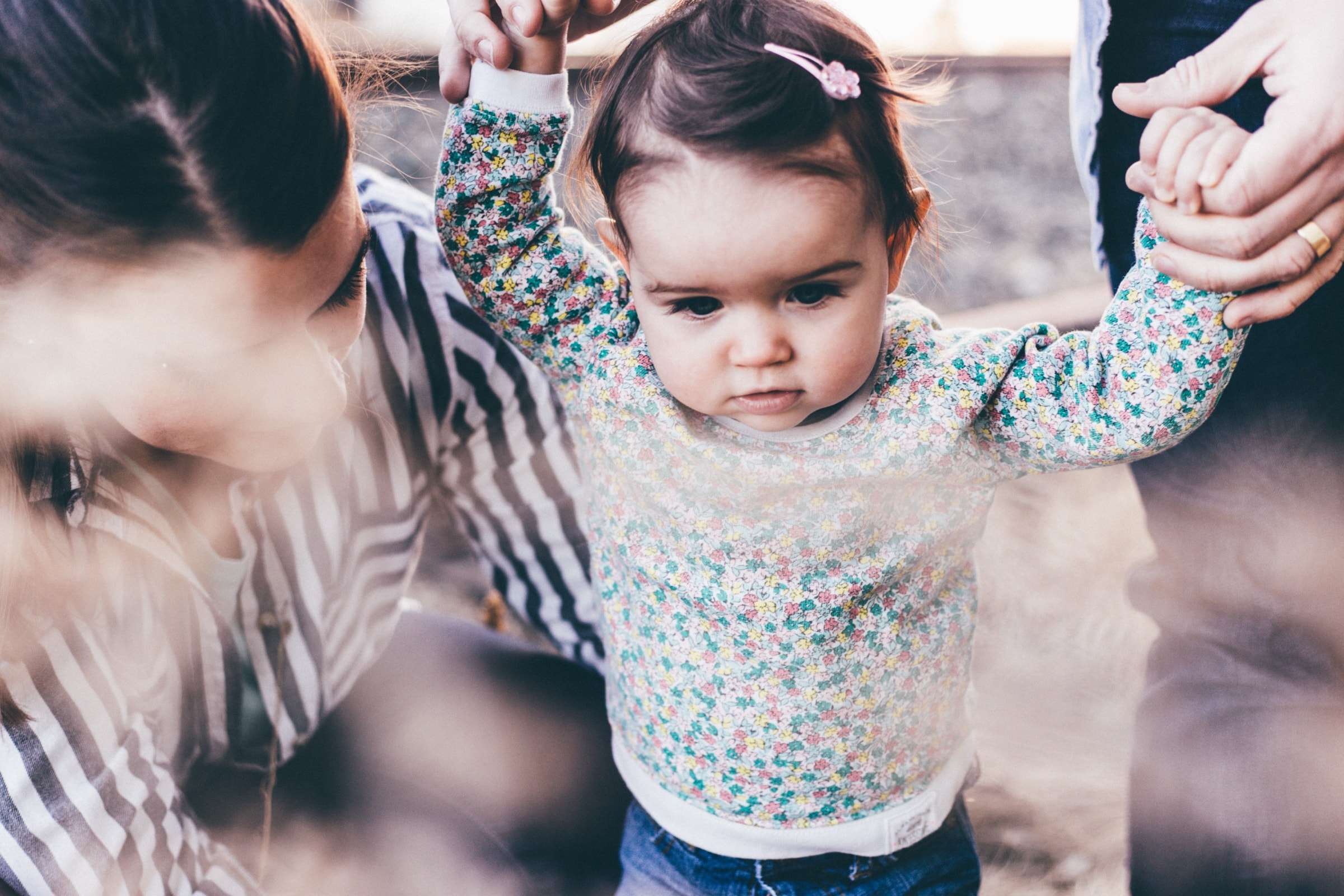 A toddler standing between two pairs of adult hands