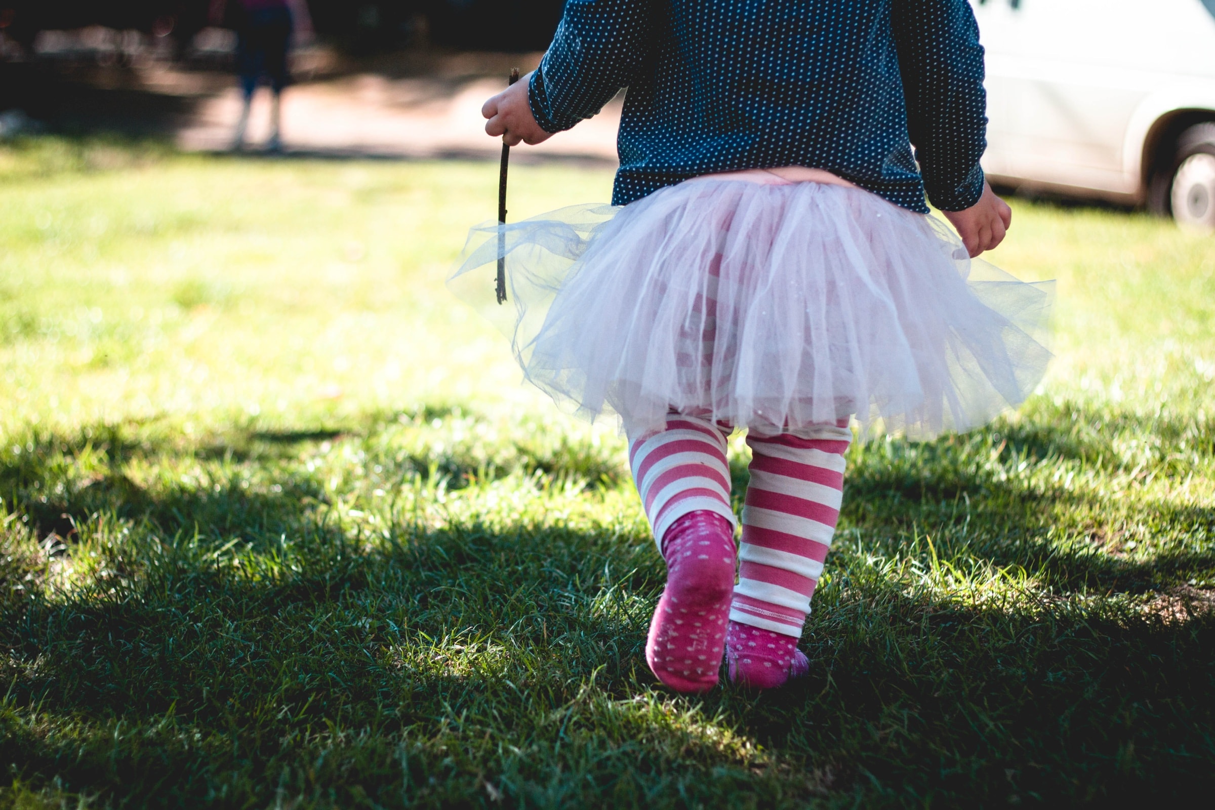 A toddler in a tutu walking across the grass